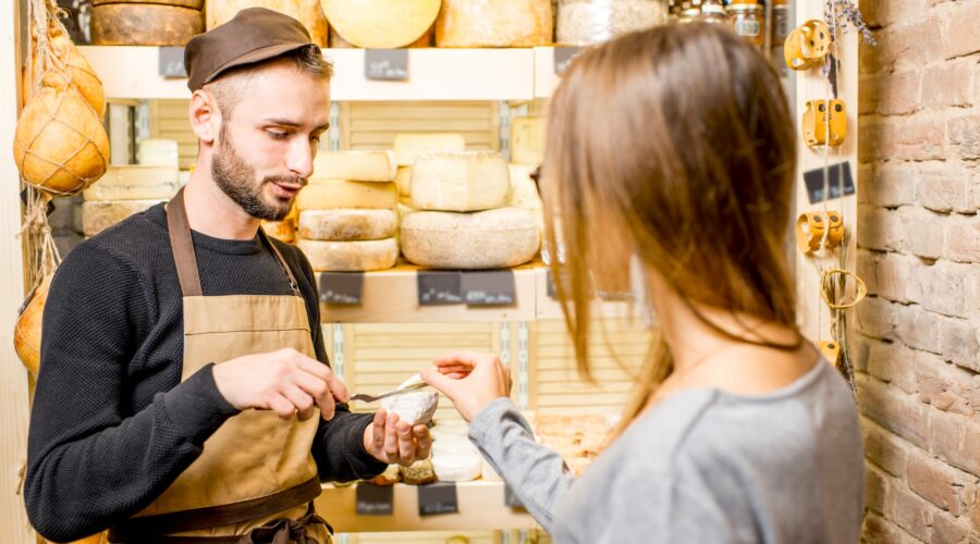 Salesman with a woman customer choosing a cheese for buying at the food store Défi entre équipes au cœur de la Grèce sauvage : Zagori, Ioannina et Metsovo